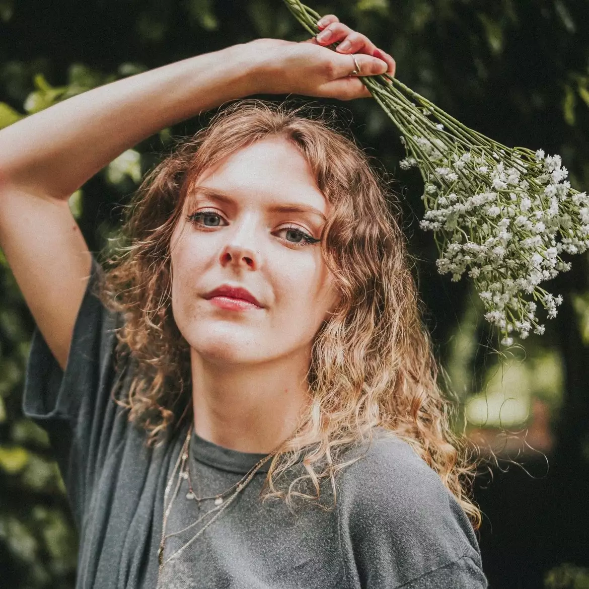Headshot of Evie Moran holding flowers over their hair