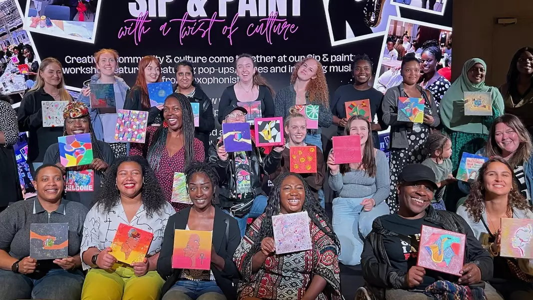 A group photo of attendees at Sip and Paint, smiling and holding their paintings up