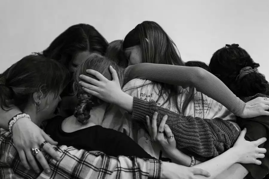 A black and white photograph of young people with their arms around each other in a group cuddle