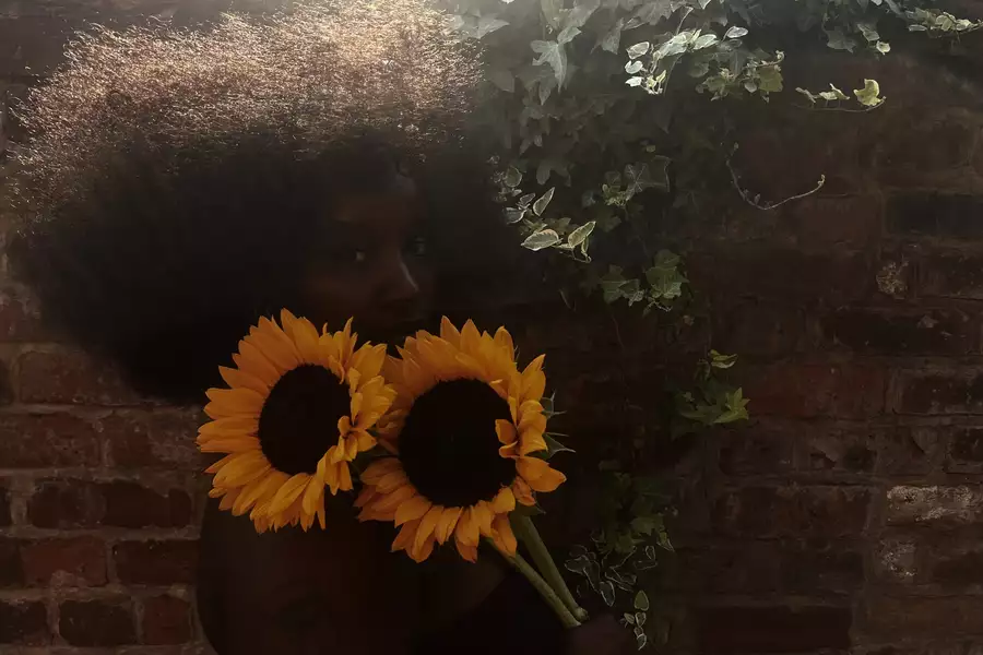 Misha B holding two sunflowers against a wall