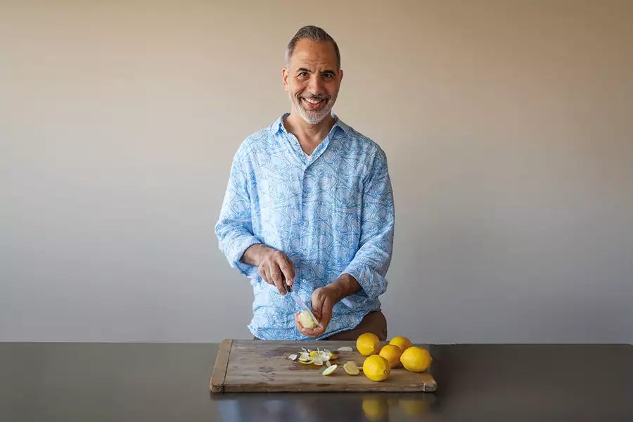 Yotam Ottolenghi wearing a light blue shirt cutting lemons on a wooden board