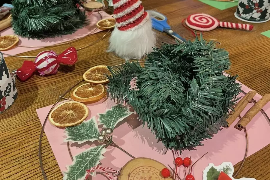 A set up for a wreath making workshop shows dried oranges, cranberries, cinnamon sticks, parts of Christmas trees, with scissors and wiring to create wreaths with.