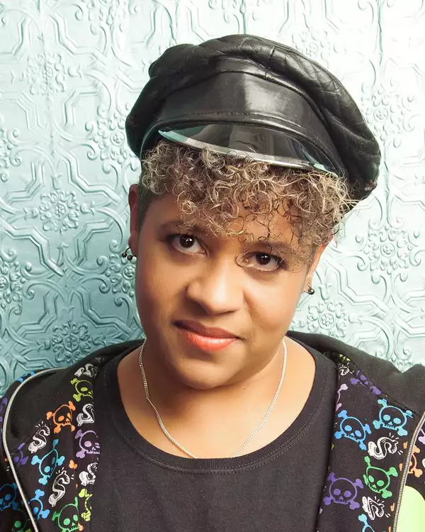 Headshot of Linda Devo wearing a black hat and jacket with brightly coloured skulls on