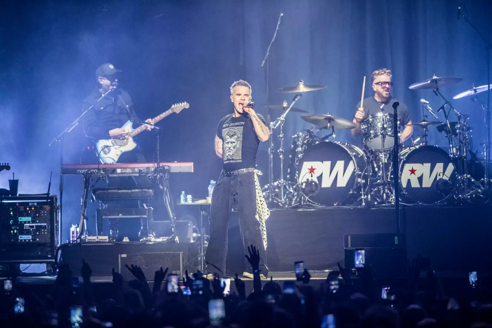 Robbie Williams on stage at Aviva Studios singing and playing guitar