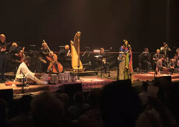 A photo of singer Jyoti Nooran smiling, she is standing on stage with Manchester Camerata at Aviva Studios