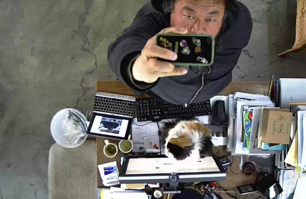 Ai Weiwei filming himself on a phone camera from above, next to a desk