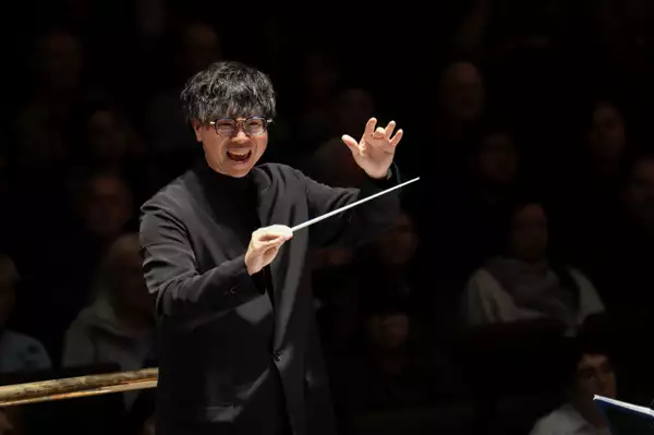 A photo of the conductor of The Halle orchestra Kahchun Wong wearing black and smiling