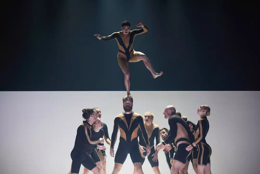 Circa acrobats performing on stage. One is balanced on top of a group of acrobats.