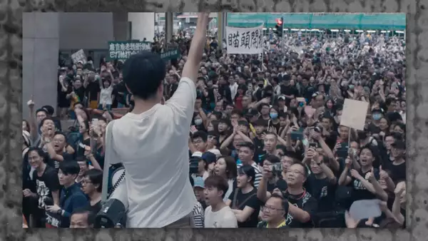 A still from Ai Weiwei's film Cockroach showing a speaker stood in front of a large crowd of people at a protest in Hong Kong