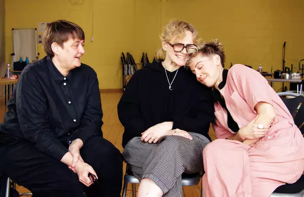 Maxine Peake, Sarah Frankcom and Imogen Knight sat on chairs smiling in a yellow rehearsal room