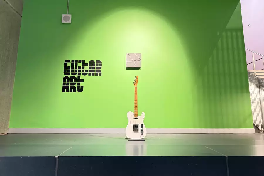 A guitar on a plinth in front of a green background.