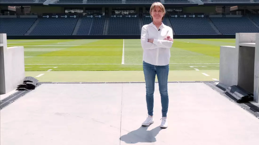 Suzanne Lacy stood on a football pitch wearing a white shirt and blue jeans