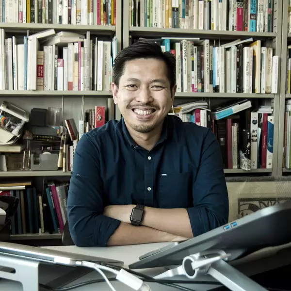 headshot of Justin Chiu-tat Wong smiling in front of a bookcase, sat at a desk