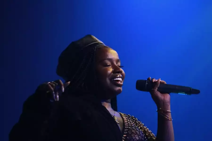 Misha B singing into a microphone on a deep blue background