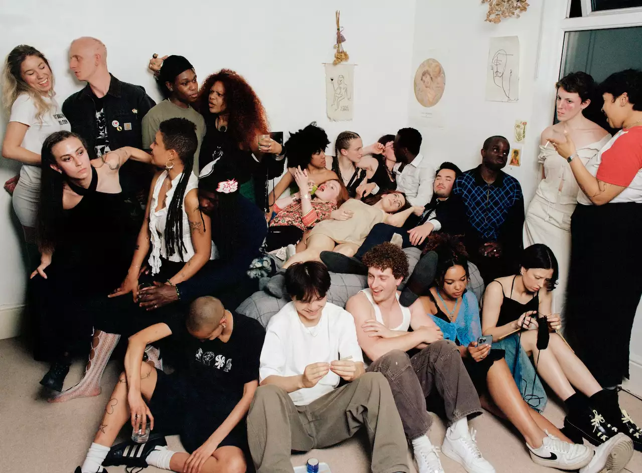 A big group of people gathered in a bedroom – sitting, standing, lying down on the bed and talking