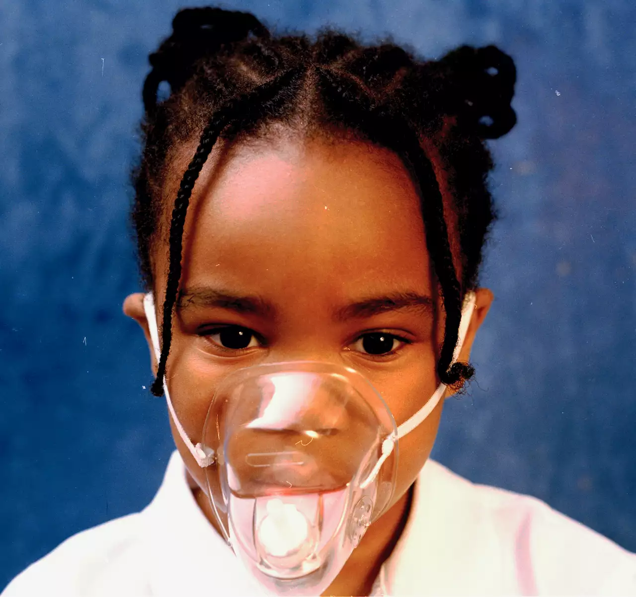 A close-up photograph of a young child wearing a clear face mask – against a blue background
