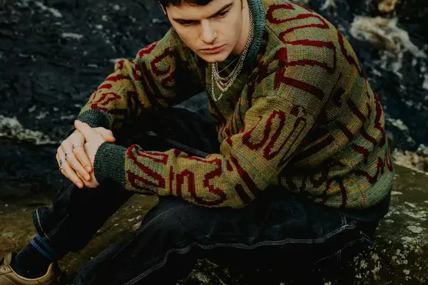 Sydney Minsky Sargeant sat on the floor outside wearing a jumper