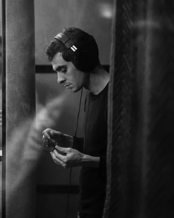 Black and white photograph of Justin Levine wearing headphones, looking down at a pair of glasses in his hands