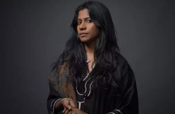 Headshot of ganavya wearing a black shirt and patterned brown scarf on a black background
