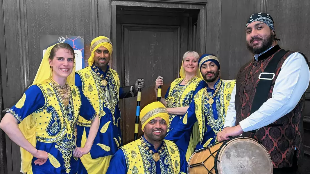 Members of Bhangracise dressed in Punjabi clothing and smiling. One is holding a drum.