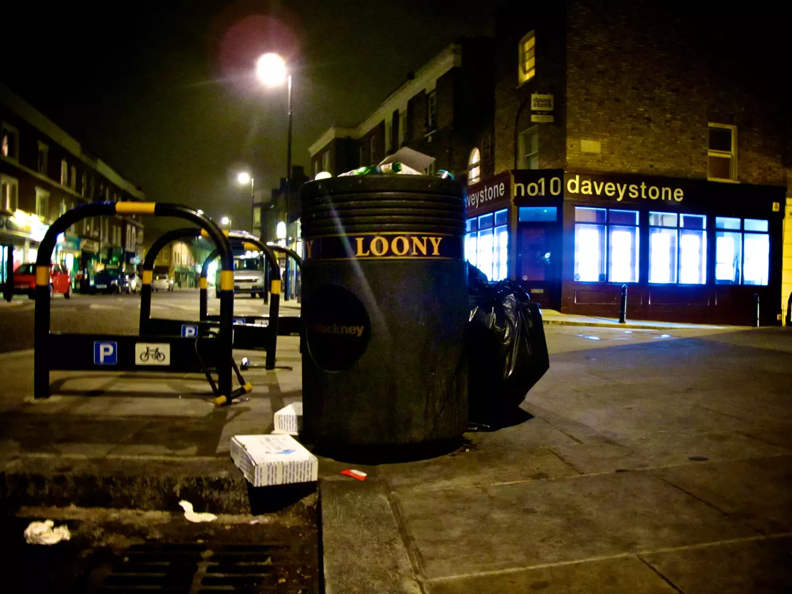 A bin on a street in Hackney with the word 'loony' on it. There is rubbish falling out the bin.