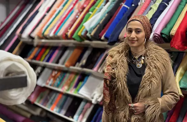 Zahra Nadeem wearing a fluffy brown coat, smiling in front of a shelf of fabrics