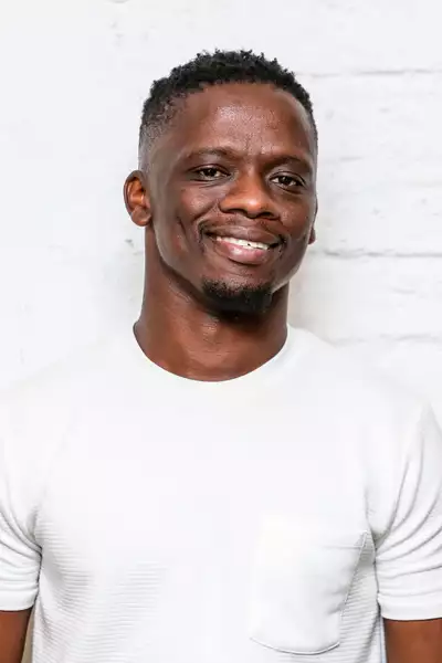 Headshot of Xoli Bongwana wearing a white t-shirt against a white brick wall
