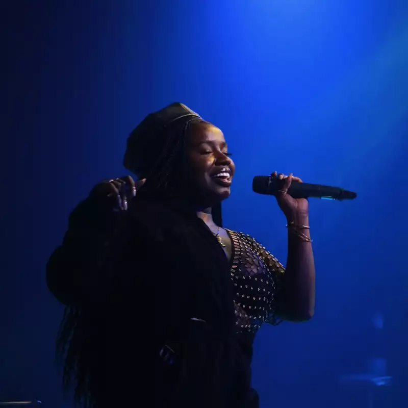 Misha B singing into a microphone on a deep blue background