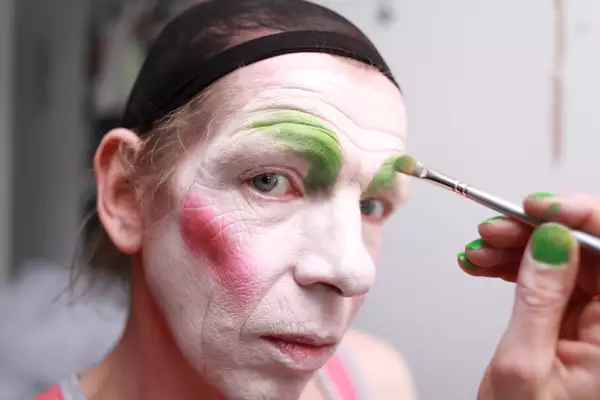Close-up photo of David Hoyle having his face painted, looking at the camera