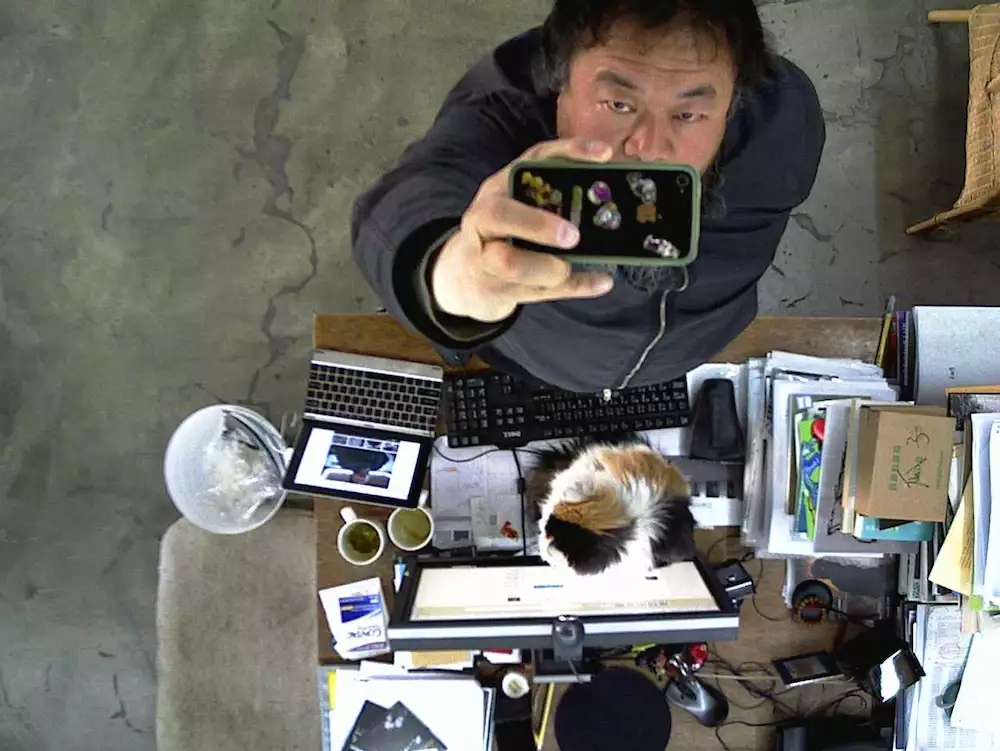 Ai Weiwei filming himself on a phone camera from above, next to a desk