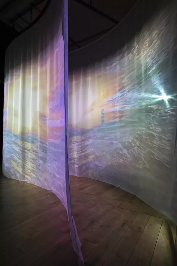 A photo of two transparent sheets of fabric hung in parallel curves with projections of waves on them