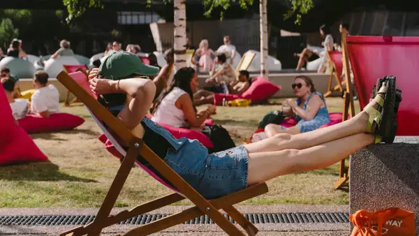 A person relaxing on a pink deck chair on grass outside Aviva Studios