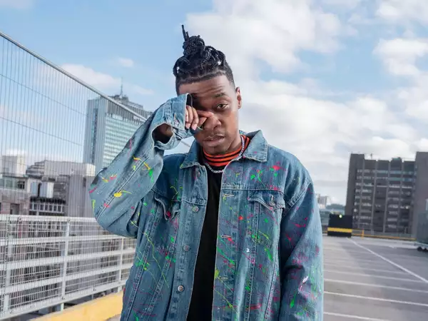 Factory Sounds 2023 cohort member PRIDO stands in a carpark wearing a denim jacket splattered with paint