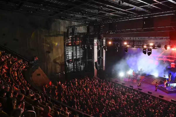 Concert crowd watching a live band perform on a brightly lit indoor stage.
