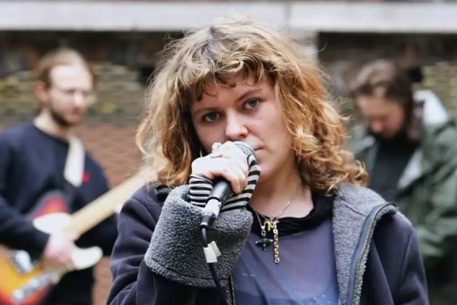 Shell Company performing outside. There is a singer in focus, and two other performers blurred out behind them.