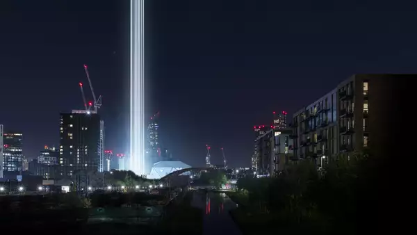 A Manchester cityscape at nighttime with bright columns of light visible next to the Factory International building.