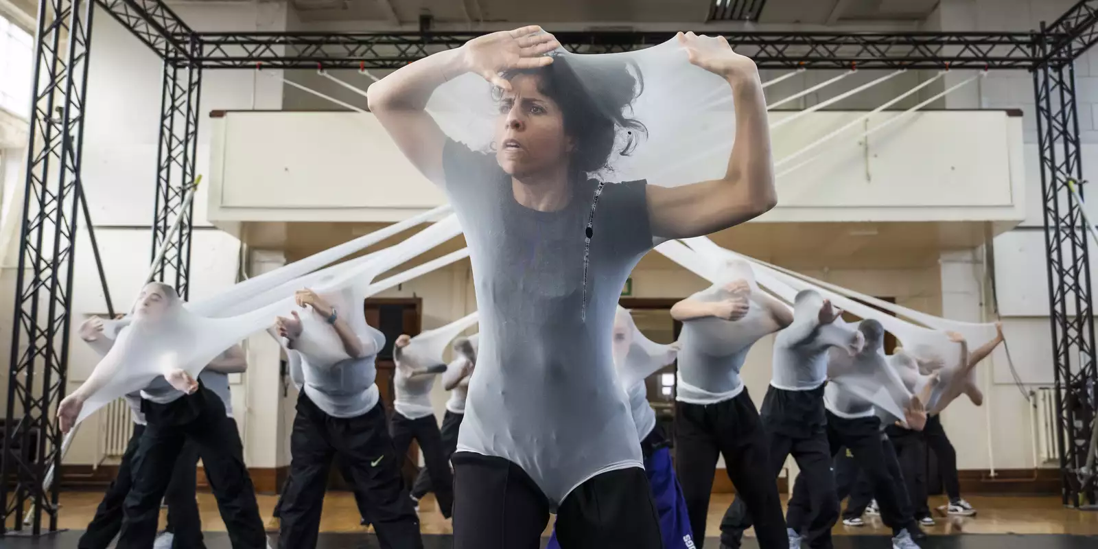 A dancer struggling to be free of stretched white fabric, more behind, in rehearsals for Free Your Mind
