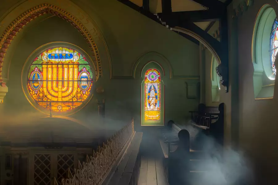 A photograph of Manchester Jewish Museum's mezzanine, with stained glass windows of a menorah and the Star of David. What appears to be mist floats through the pews.
