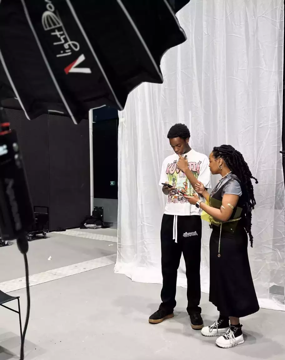Two people looking at their phones, stood in front of a white drape of material