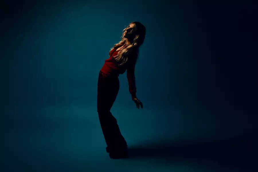 Agnes Obel standing in a blue room, bending her body and looking upwards
