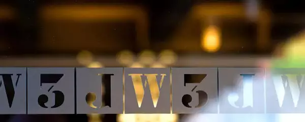 Close-up of illuminated letterpress-style letters on glass, spelling JW3, with warm lights in the background.