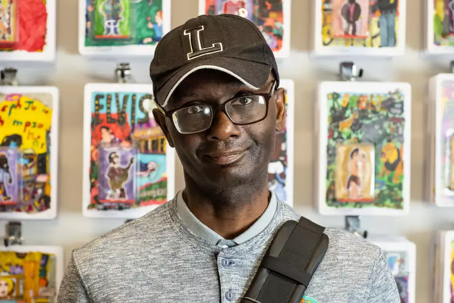 Leslie Thompson wearing a black cap with an 'L' on, stood in front of a wall of artwork