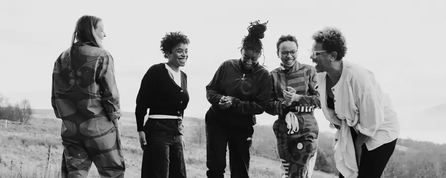 Black and white photograph of five people stood up laughing and smiling