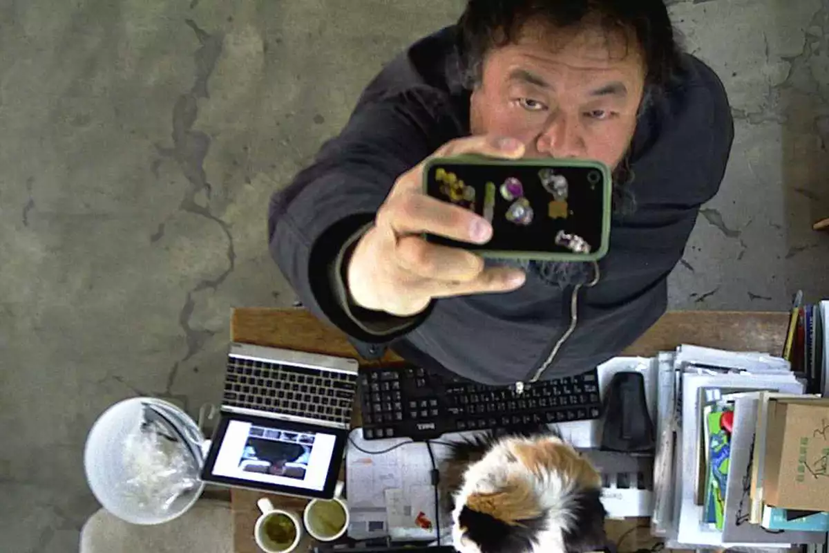 Ai Weiwei filming himself on a phone camera from above, next to a desk
