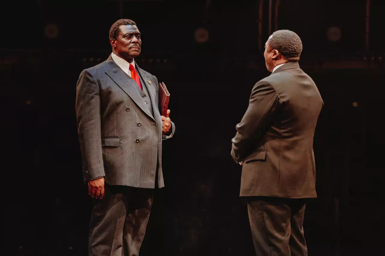Two actors on stage at Liberation, wearing suits mid-conversation