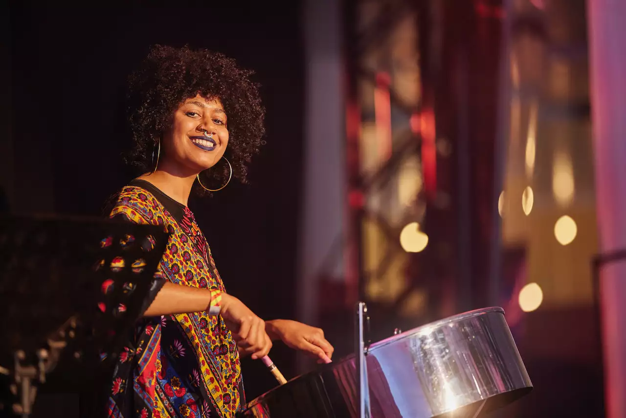 Photo of Zola Tec smiling and playing the steel drum on stage