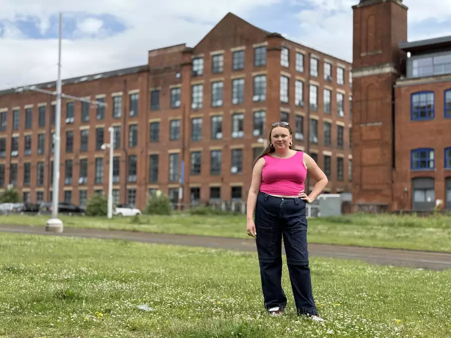 Ellie Brown wearing a bright pink top and jeans, stood outside a converted mill on the grass