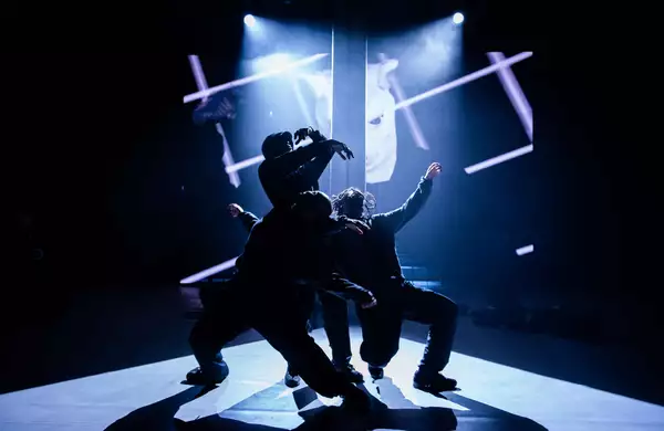 Three dancers dancing on stage around a pole during Traplord, with a projection behind them.