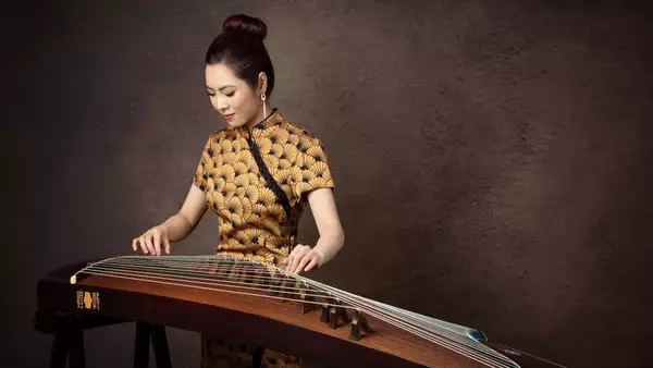 Belle playing the guzheng – against a brown background