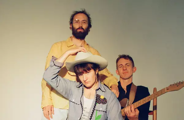 Three members of Big Thief on a white background. Adrianne Lenker is wearing a white cowboy hat.